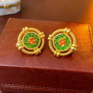 Close-up of vintage gold earrings with green and orange gemstones on a leather box