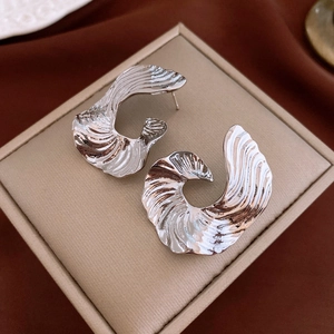 Macro detail of silver-toned metal earrings with wavy texture on jewelry box