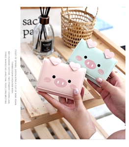 Cute cartoon pig wallets in pink and mint green displayed on a wooden tray with a lifestyle theme