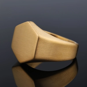 Macro view of a gold hexagonal signet ring featuring a matte brushed metal texture finish