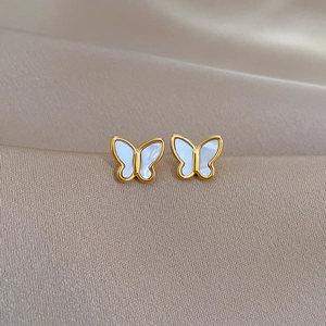 Macro shot of gold butterfly stud earrings with white inlay on champagne silk fabric