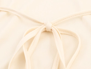 Close-up detail of the elegant beige knit dress featuring a delicate lace-up back design