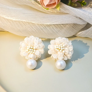 Detailed shot of white lace flower earrings with soft pearls on silk fabric background