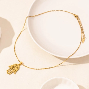 Close-up of golden stainless steel necklace featuring a hollow Hamsa Hand pendant on a plate