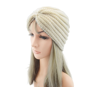 Close-up of beige knitted turban hat with pleated design on a white background