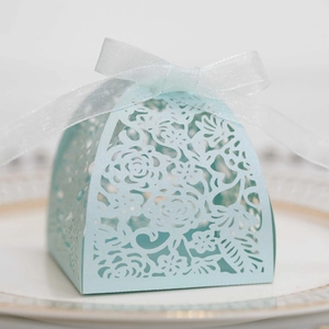 Close-up of light blue laser-cut wedding favor box with rose pattern and white ribbon