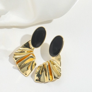 Detailed view of gold maple leaf earrings with black oval inlay on white silk fabric