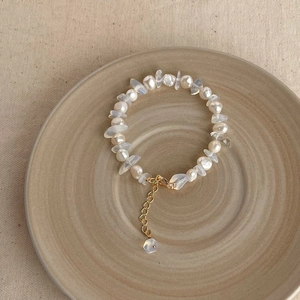 Baroque natural pearl bracelet with golden clasp on a beige ceramic plate and linen fabric