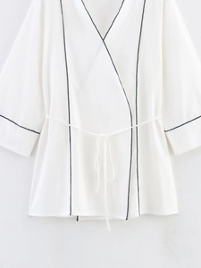 Detailed view of white long sleeve jacket featuring black piping and an adjustable waist tie
