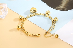 Détail du bracelet double chaîne doré orné de breloques en cœur et de perles polies