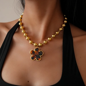Close-up of golden beaded sweater necklace featuring a vintage flower pendant with amber inlay