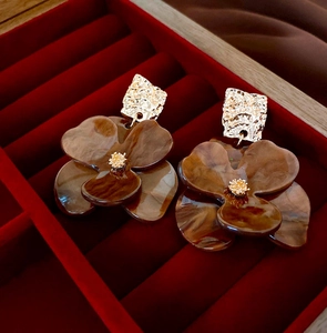 Macro shot of brown resin flower earrings with gold metal details on red velvet background