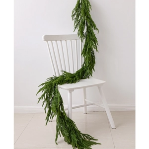 Lifelike green Norfolk pine garland draped on a white chair for Christmas home decoration