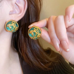 Close-up of vintage gold round earrings with green enamel and floral relief design