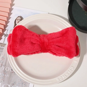 Close-up of a soft red coral fleece headband with a large bow on a ceramic plate