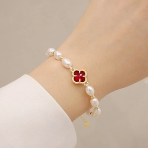 Detail of a pearl bracelet with red clover pendant on a female model's wrist
