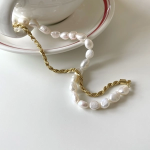 Baroque pearl and golden rope chain necklace elegantly draped over a white ceramic cup