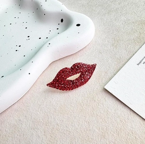 Sparkling red lip brooch with rhinestones on a minimalist textured tabletop