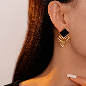 Close-up of vintage geometric woven earrings with black tiles and gold bead tassels