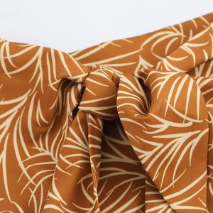 Brown resort dress with white palm leaf print and a front knot bow detail