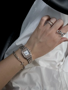 Close-up of a ladies' square diamond watch with roman numerals and matching silver rings