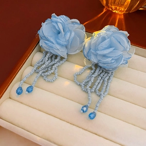Detail of light blue fabric flower earrings with beaded tassels on jewelry tray