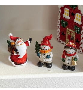 Close-up of resin Santa Claus and snowmen figurines with snowy red house backdrop