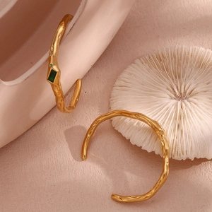 Detail of 18K gold-plated irregular textured cuff with green zircon on a pink ceramic base