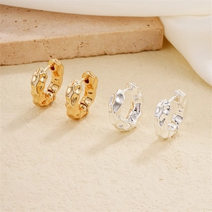 Irregular textured metal hoop earrings in gold and silver finish on silk background