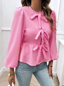 Detailed close-up of pink long-sleeve blouse featuring textured fabric and front bow ties