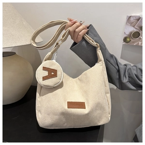 Detail of beige corduroy tote bag with letter A coin purse charm held by a model