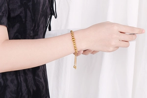Detail of a gold beaded adjustable bracelet on a model's wrist with a slider clasp