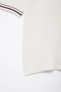 Detailed macro view of cream-white cable knit texture and striped ribbed cuff on polo top