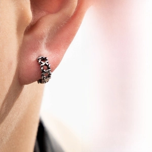 Macro view of vintage silver earring with embossed X patterns on an ear model