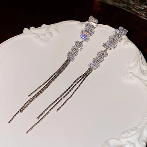 Detail of silver tassel earrings with rectangular zircons on a white ceramic plate
