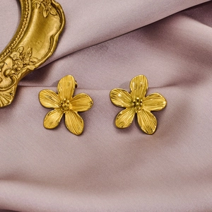 Elegant gold flower stud earrings with five-petal design on purple satin background
