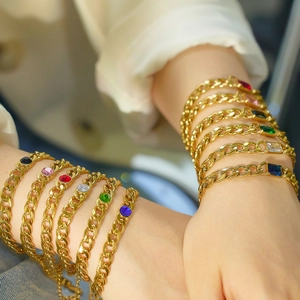Close-up of gold Cuban chain bracelets with multi-colored gemstones on a model wrist
