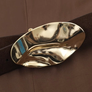 Détail de la boucle en métal doré en forme de feuille sur une ceinture marron foncé