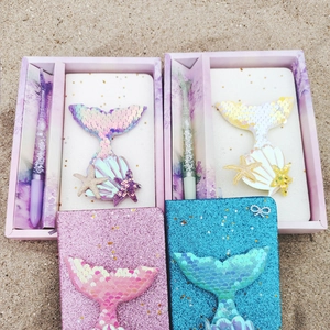 Mermaid stationary set with sequin notebook and sand pen on a sandy beach background