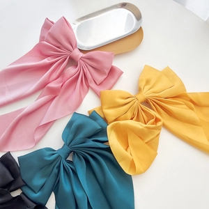 Close-up of four glossy satin bow hair clips in pink, yellow, green, and black