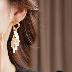 Golden round earrings with white shell tassel petals shown on model for resort fashion