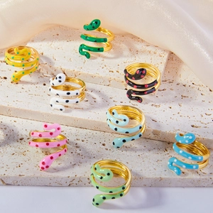 Stacked gold-plated snake rings with colorful enamel dots on a minimalist stone display