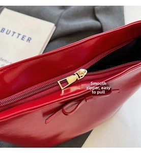 Detail of red patent leather handbag featuring a gold zipper and decorative bow