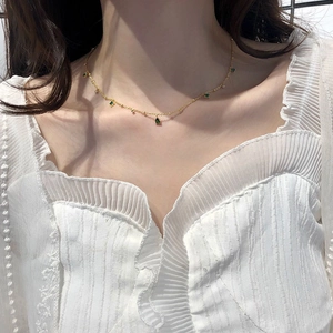 Close-up of gold collar necklace with green emerald-like gemstones on female neck