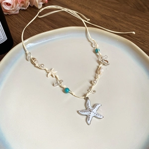 Detail view of a shell and starfish necklace on a ceramic plate with coastal vibes