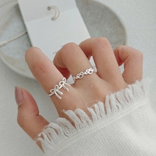 Detail showing two silver bow rings with zircon stones worn by a model in a cozy setting
