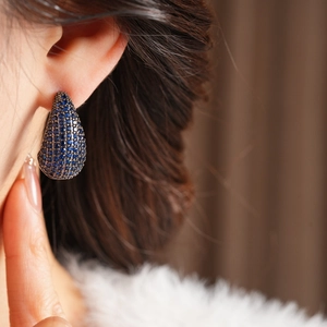 Close-up of vintage teardrop earrings featuring deep blue pavé zircon on model