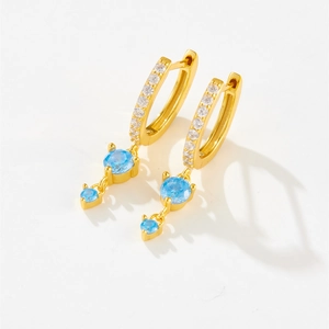 Macro detail of gold earrings featuring light blue round zircons and micro-pave white stones