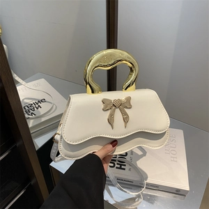 Modern white leather handbag with wave flap and gold bow accent held by metal handle