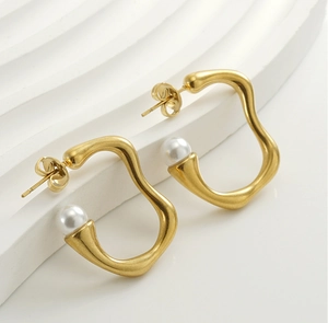 Détail de boucles d'oreilles dorées mates irrégulières avec perles blanches sur socle